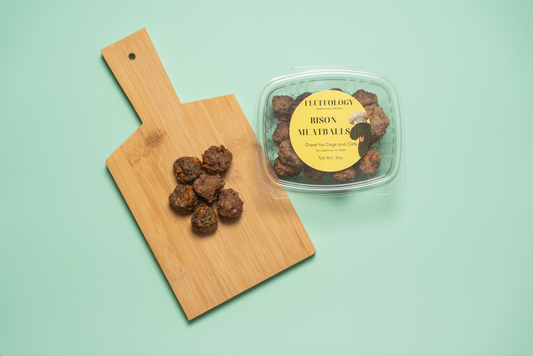 Bison meatballs on a wooden cutting board with a container labeled 'Fulfilment' on a light green background. Fluffology Bison Meatballs
