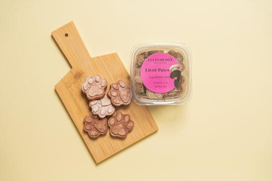 Dog treats shaped like paws on a wooden board with a container labeled 'Liver Paws' on a beige background. Fluffology Freeze Dried Beef Liver Paws